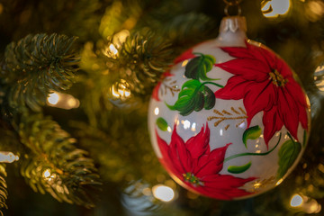 A poinsettia adorned ornament hanging from a festive Christmas tree.