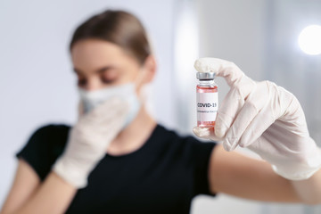 Bottle of corona virus COVID-19 vaccine in hand of woman patient in disposable facial mask. Coronavirus 2019-nCoV concept.