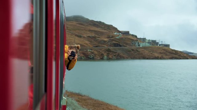 Cinematic and movie like video of woman hang out of train window. Young female traveler makes photos from open window of red swiss bernina train. Inspiring original and authentic travel destination