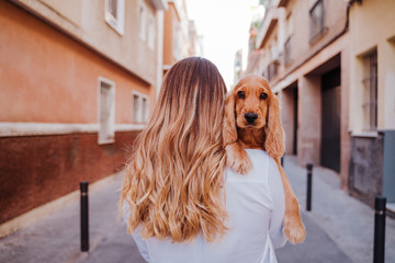 young woman at the street holding with her cute cocker dog on shoulder. Lifestyle outdoors with pets