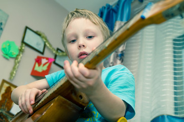 A boy European 5 6 years learn play on old guitar. Happy toddler baby loves to sing and play the instrument. Development of the child's talent.