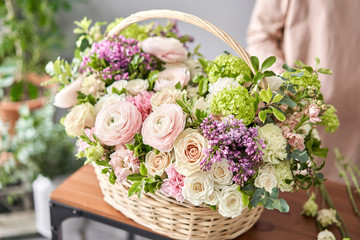 Floral shop concept . Florist woman creates flower arrangement in a wicker basket. Beautiful...