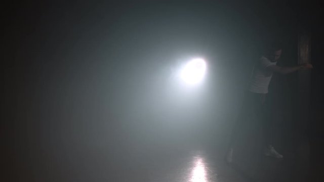 Guy jumping double sideflip on floodlight background in slow motion. Night tricking, making kick. Man demonstrates extreme tricks in smoke dark studio 