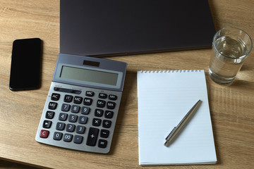 Remote work laptop calculator phone notepad with pen and glass of water on the table