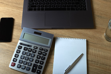 Remote work laptop calculator notepad with pen and glass of water on the table