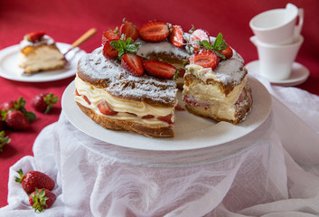 Delicious strawberries cream cake decorated with fresh cut strawberries on a white plate on the red background.