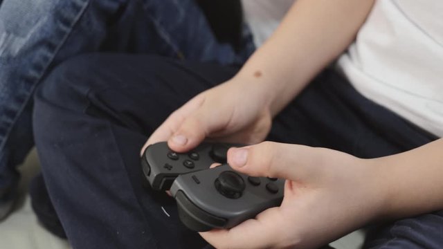 Blonde-haired children a girl and a boy play a game console. Happy children play sitting on a white sofa at home. Large console