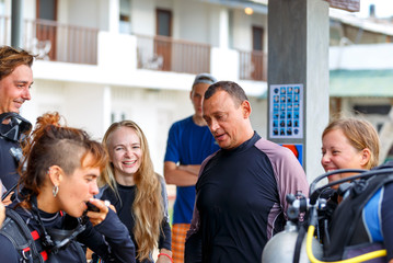Group of scuba divers on the beach listening to instructions before the dive. female divers in dive gear smile and laugh at the briefing before swimming.