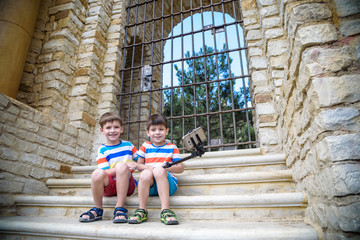 Two cute little brothers sitting on stairs in Italian town. Make selfie on mobile phone. Kids...