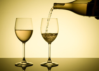 Two glasses of white wine. Wine is poured into a glass from a bottle. Yellow background. Alcohol drink. 