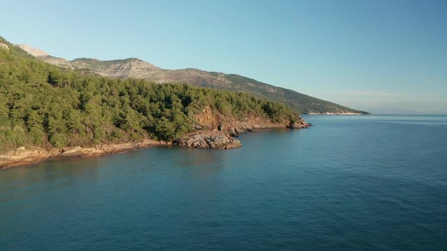 Drone flight around the mountain slopes and rocky coastline of Thasos island and the little island Nisida Kinira, Greece
