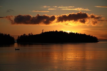 sunset of the outgoing day over the island and a lone fisherman on the lake