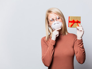 Style blonde woman in face mask with gift box on white background