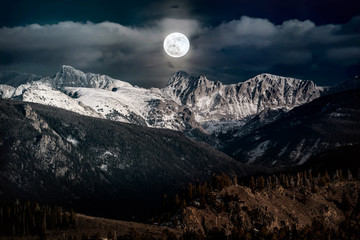 Snow peaked mountains under a full moon night sky at Rocky Mountains National Park, Colorado USA.
