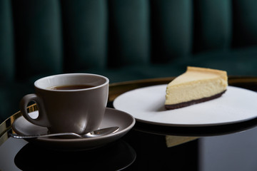 Cup of tea and slice of cheesecake on white plate on table