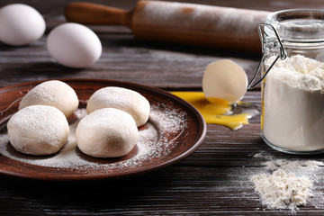 Four balls of dough on a plate, on a wooden background, with eggs, a jar of flour, and with a rolling pin. The process of making dough.
