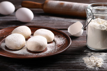 Four balls of dough on a plate, on a wooden background, with eggs, a jar of flour, and with a rolling pin. The process of making dough.