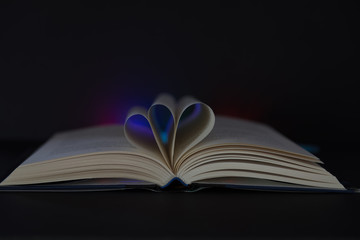 An open book with curved pages on a black background and illuminated by colored light.