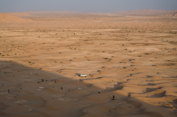 Above view of endless sand dunes in desert and small white car near the shadow border