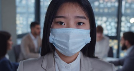 Close up face portrait of a young asian business woman wearing protective mask looking at camera in office. Concept of health and safety life, coronavirus, virus protection, pandemic. - Powered by Adobe
