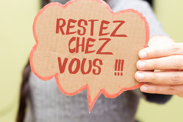 closeup woman hand holding speech card bubble with french word restez chez vous translated in...