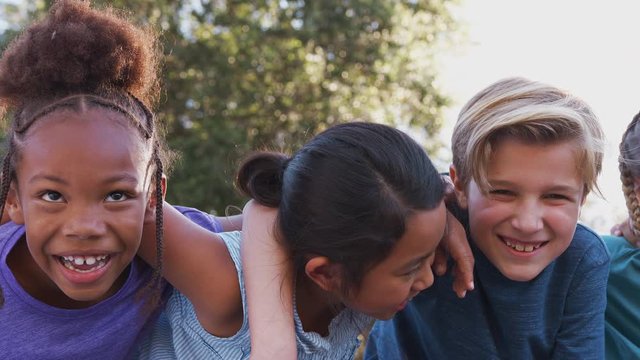Camera tracks along faces of group of children hanging out with friends outdoors with arms around each other - shot in slow motion