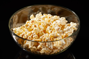 Glass bowl with salted popcorn with cheese. Heap of homemade delicious popcorn on a rustic wooden table. Snacks and food for a movie theater or cinema. Fastfood background. TV remote control