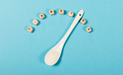 Word diabetes in block letters on cubes and teaspoon with sugar, blue background, concept
