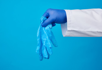 male hand holds a pair of medical latex medical gloves on a blue background