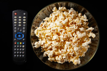 Glass bowl with salted popcorn with cheese. Heap of homemade delicious popcorn on a rustic wooden table. Snacks and food for a movie theater or cinema. Fastfood background. TV remote control