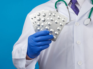 male hand with blue sterile gloves holds a stack of pills in a blister