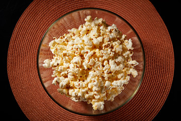 Glass bowl with salted popcorn with cheese. Heap of homemade delicious popcorn on a rustic wooden table. Snacks and food for a movie theater or cinema. Fastfood background. TV remote control
