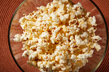 Glass bowl with salted popcorn with cheese. Heap of homemade delicious popcorn on a rustic wooden table. Snacks and food for a movie theater or cinema. Fastfood background. TV remote control