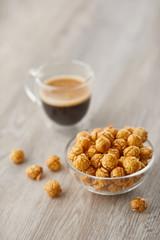 Appetizing caramelized popcorn and cup of coffee. Heap of homemade delicious popcorn on a wooden background. Snacks and food for a movie theater or cinema. Fastfood background.