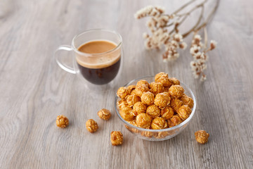 Appetizing caramelized popcorn and cup of coffee. Heap of homemade delicious popcorn on a wooden background. Snacks and food for a movie theater or cinema. Fastfood background.