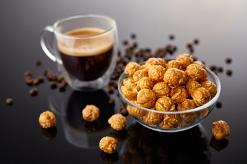 Appetizing caramelized popcorn and cup of coffee. Heap of homemade delicious popcorn on a black mirror background. Snacks and food for a movie theater or cinema. Fastfood background.