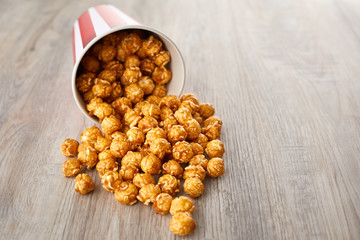 Appetizing caramel popcorn in the paper cup. Heap of homemade delicious popcorn on a wooden background. Snacks and food for a movie theater or cinema. Fastfood background.