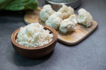Cauliflower rice on a wooden bowl with some pieces of cauliflower in background. Healthy and raw product. Close up view.