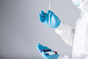 virologist in a protective suit with a respiratory face mask and blue gloves holds a syringe and...