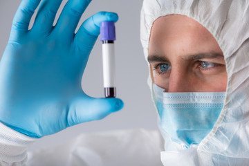 A virologist in a medical mask and protective clothing holds a test tube with a blood sample for coronavirus testing. Pandemic. Respiratory syndrome, panic, experiences, research