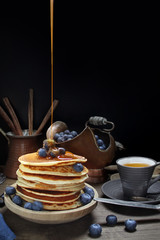 national dish pancakes, pancakes, pita with blueberries, honey pours on food, a linen napkin, a candle burns, a cup of tea, an old mocha coffee machine, a concept of traditional cuisine