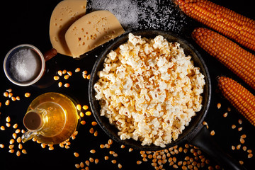Appetizing salted popcorn with cheese. Heap of homemade delicious popcorn on a rustic wooden table. Snacks and food for a movie theater or cinema. Fastfood background. Frying pan with corn and oil. .
