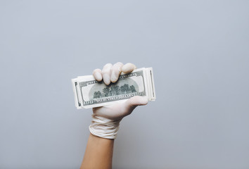 A man holds money in white medical gloves. Isolated. Gray background. The concept of treatment...