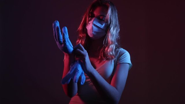 Young woman wearing a medical face mask and putting on protective gloves to minimize risk of coronavirus
