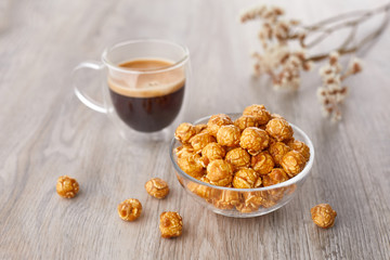 Appetizing caramelized popcorn and cup of coffee. Heap of homemade delicious popcorn on a wooden background. Snacks and food for a movie theater or cinema. Fastfood background.