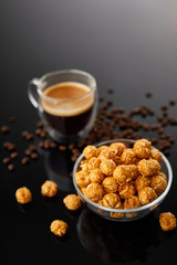Appetizing caramelized popcorn and cup of coffee. Heap of homemade delicious popcorn on a black mirror background. Snacks and food for a movie theater or cinema. Fastfood background.