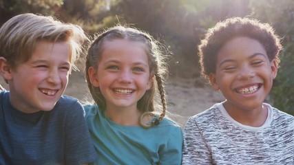 Camera tracks along faces of group of children hanging out with friends outdoors with arms around each other against flaring sun - shot in slow motion - Powered by Adobe