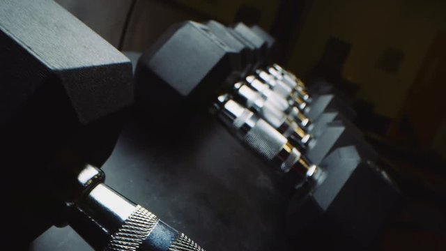 Low macro shot moving across weights as woman picks up dumbbell in moody gym