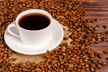 A cup of black aromatic coffee in a white cup on a background of roasted coffee beans arabica coffee on a wooden table