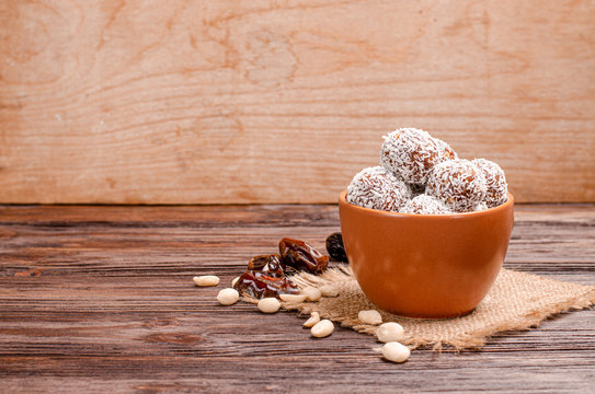 Energy balls from dates, peanuts, oats, sprinkled with coconut in a clay brown cup close-up on a wooden background with copy space